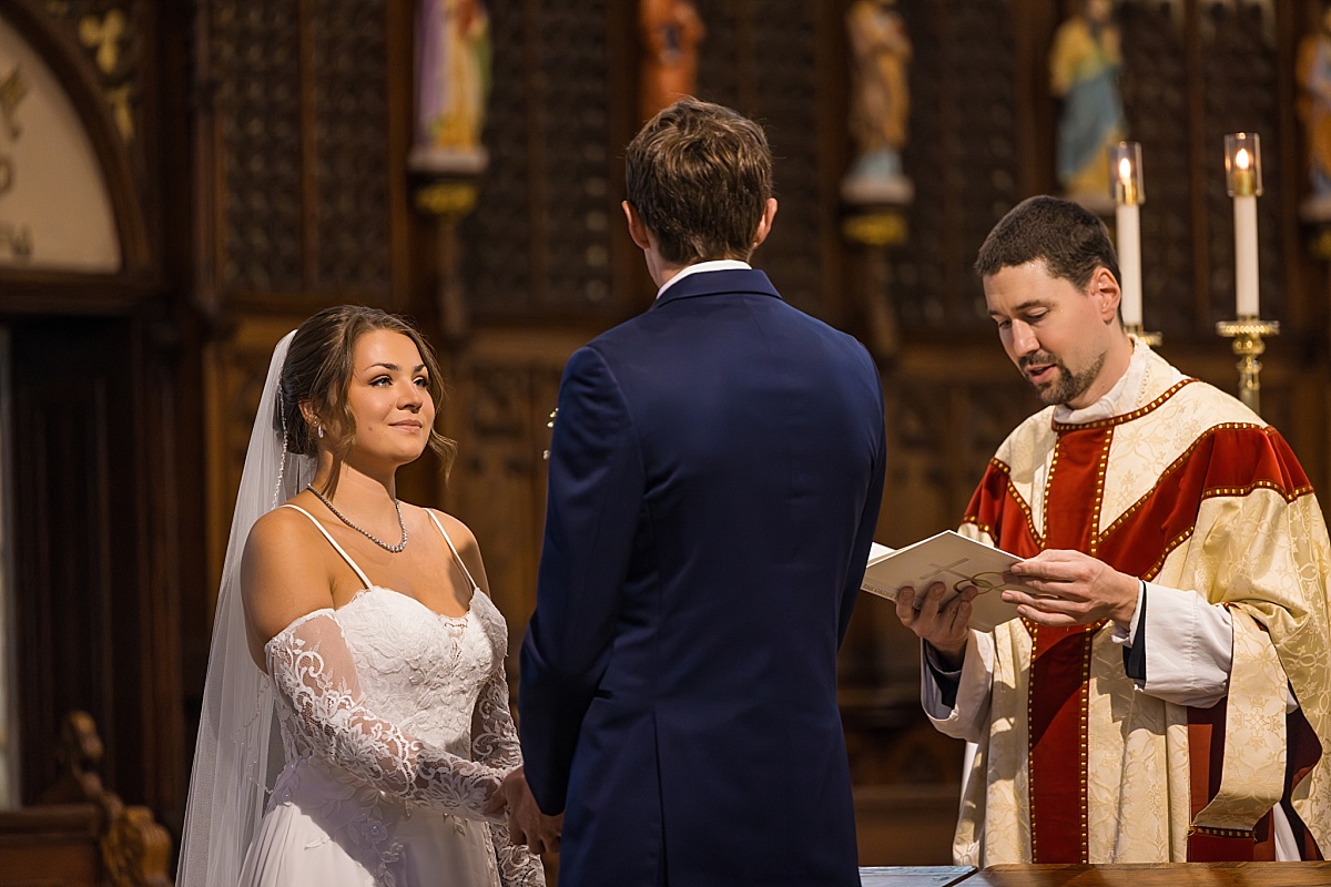Grace and Alex hold hands during their wedding ceremony at Ste. Genevieve Catholic Church