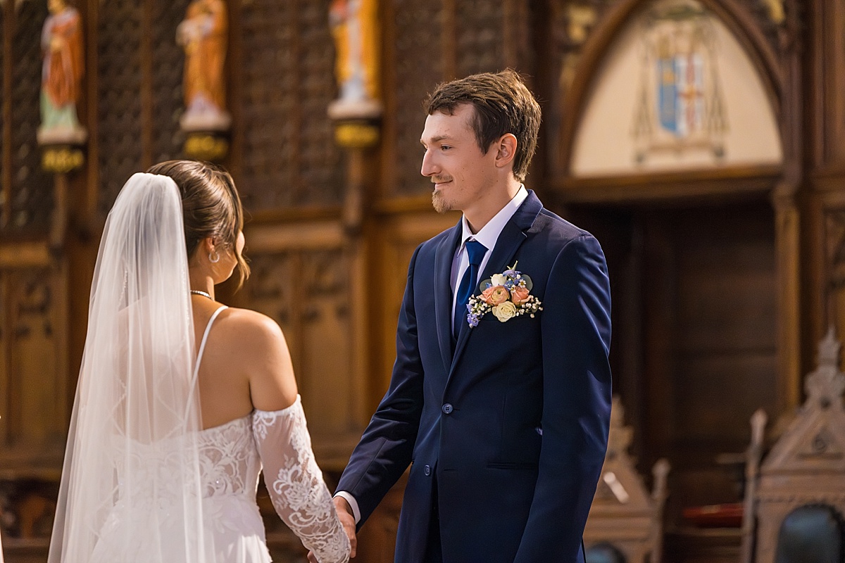 Grace and Alex hold hands during their wedding ceremony at Ste. Genevieve Catholic Church