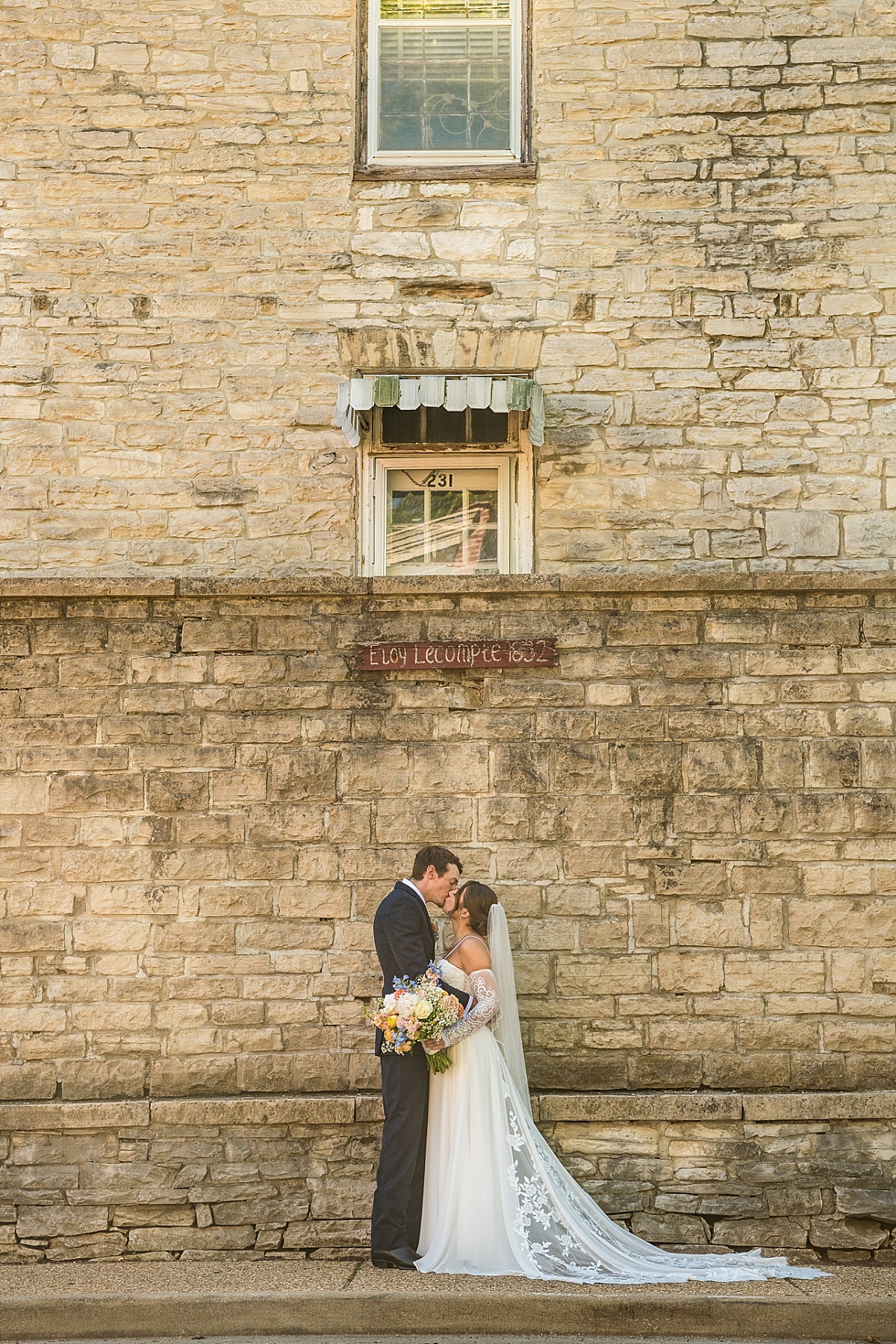 Grace and Alex kiss beside a historic stone building in downtown Ste. Genevieve
