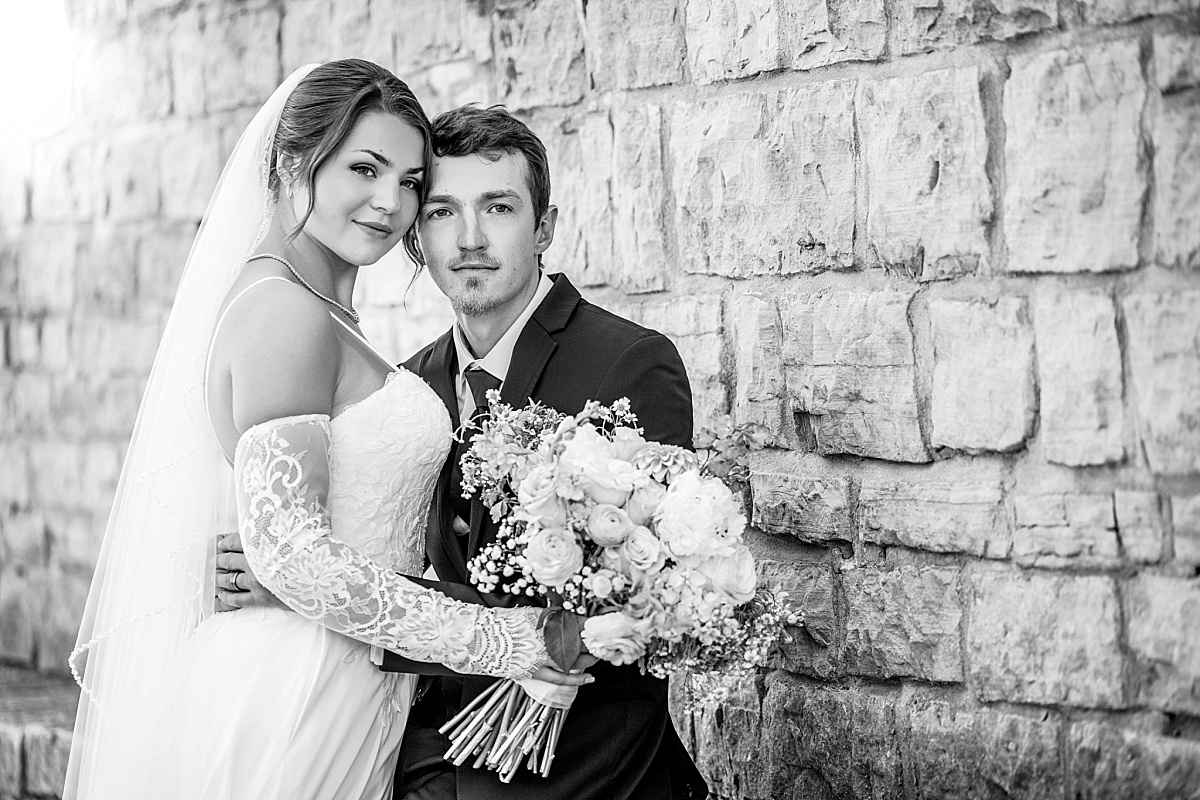Black and white close portrait of Grace and Alex by a historic stone wall