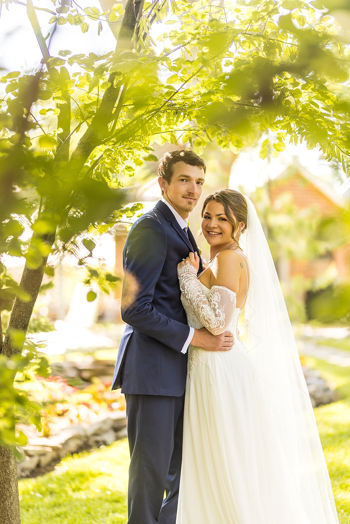 Grace and Alex smile together under the trees during their wedding portraits