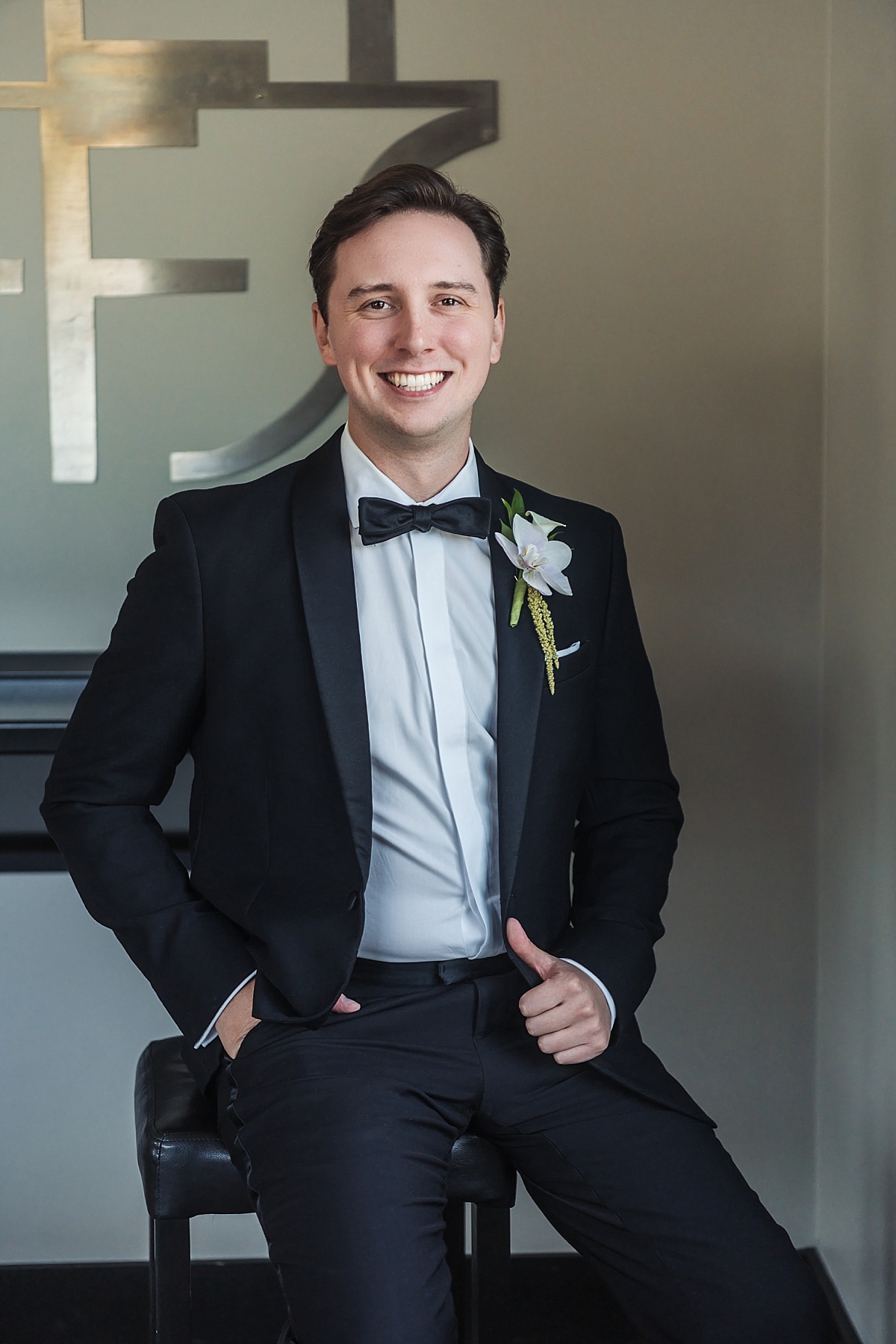 Groom Justin smiles in his black tuxedo and orchid boutonniere before the wedding ceremony.