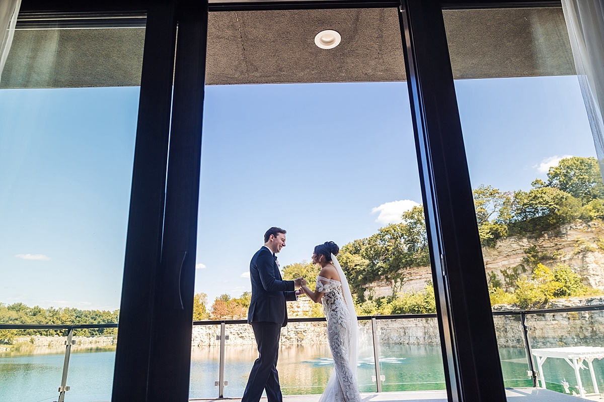 Melicia and Justin hold hands by the windows overlooking the lake at Sunset Bluffs.