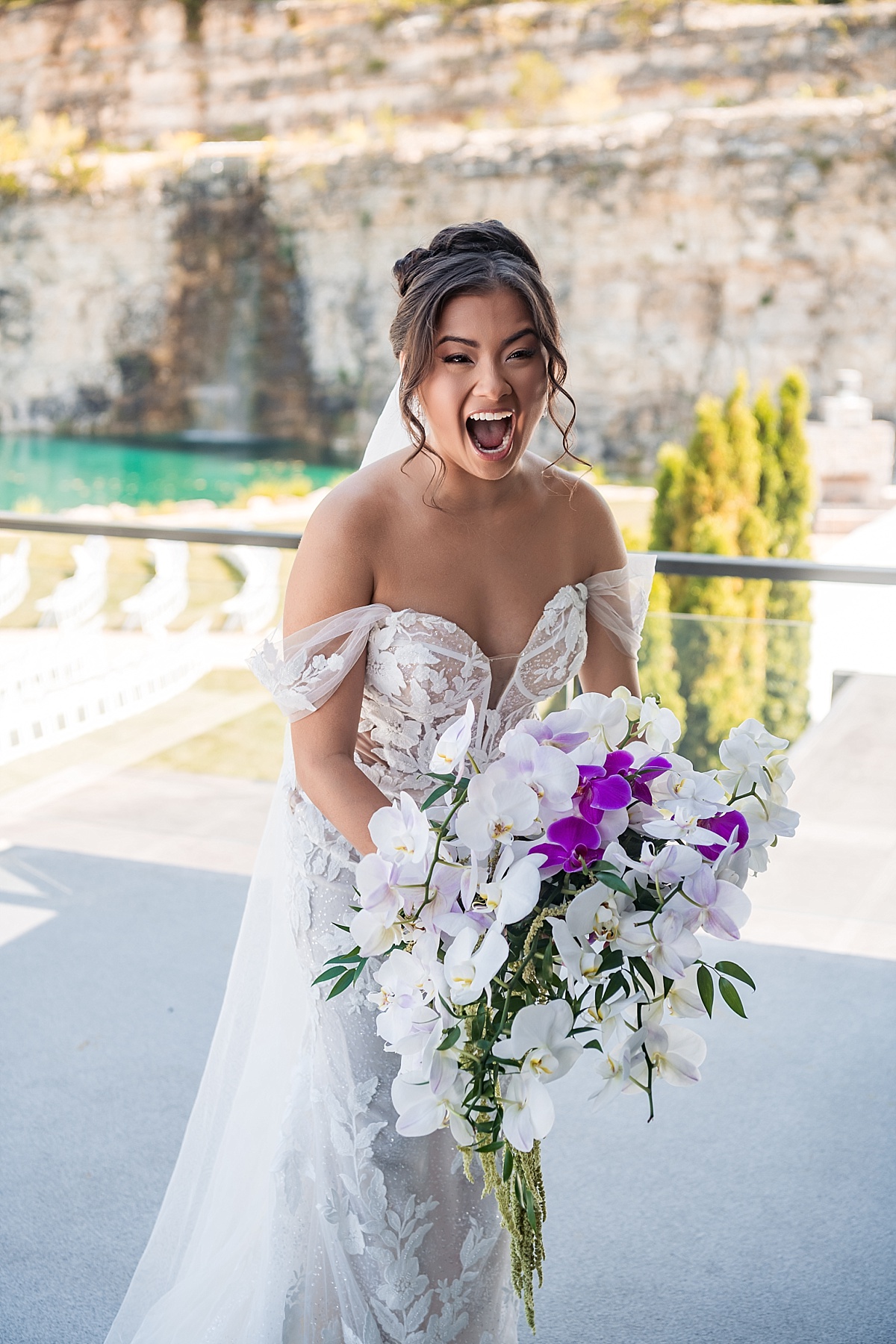 Melicia laughs with excitement in her lace wedding dress while holding her white and purple orchid bouquet.