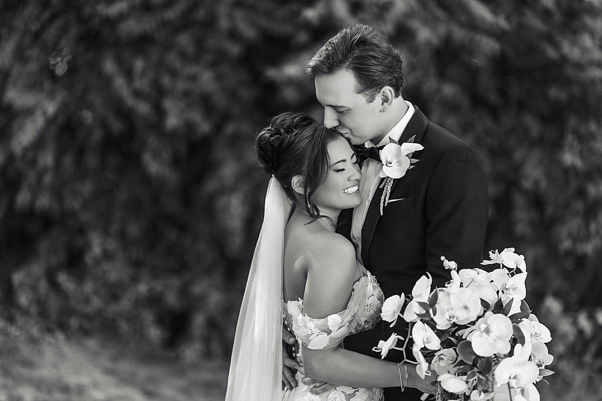 Black-and-white portrait of Justin kissing Melicia on the forehead as she smiles in his arms.
