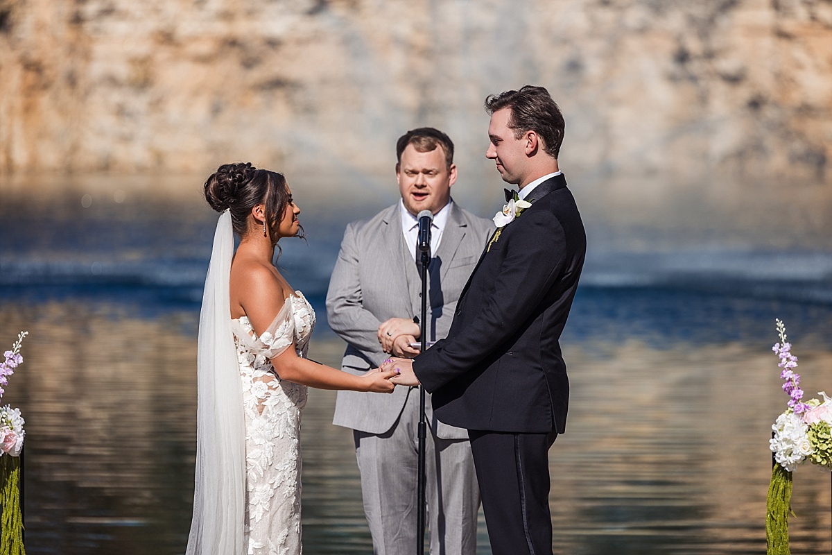 Melicia and Justin hold hands as their officiant leads their wedding ceremony beside the water.