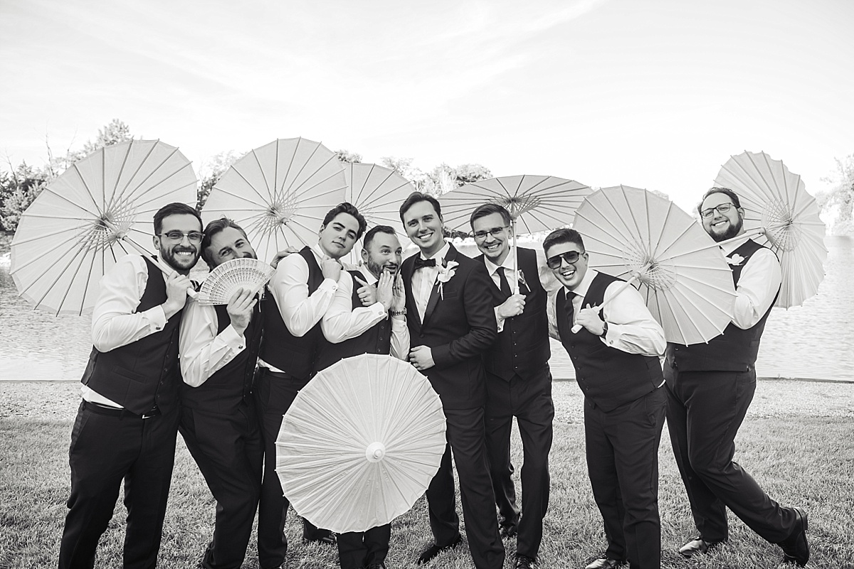 Justin and his groomsmen pose playfully with white parasols in a black-and-white wedding party portrait.