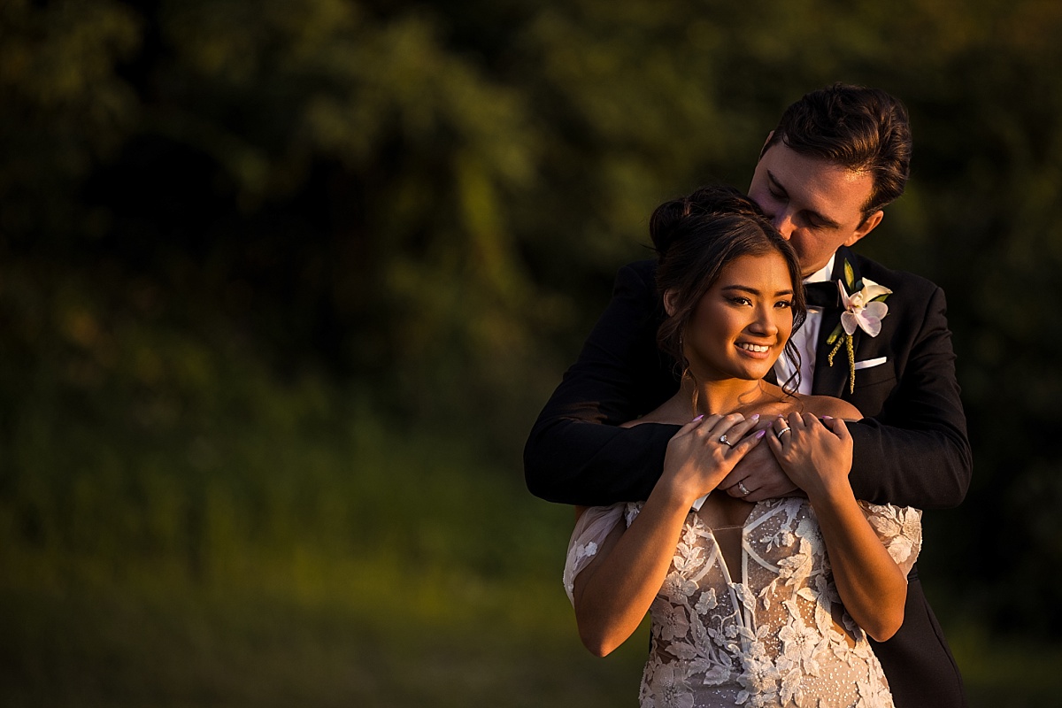Justin wraps his arms around Melicia from behind during a romantic portrait in warm evening light.