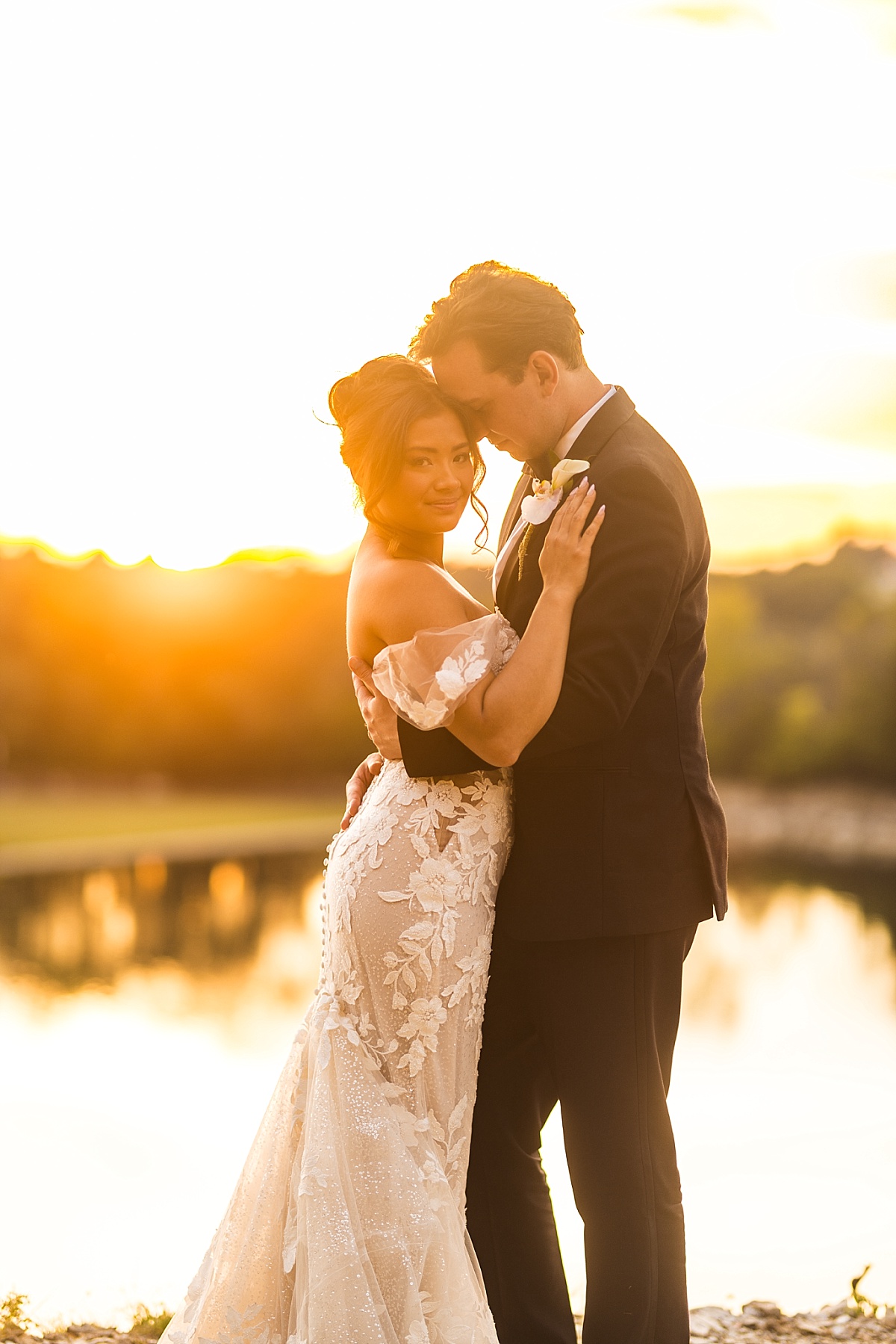 Melicia and Justin embrace beside the lake as the setting sun casts a golden glow around them.