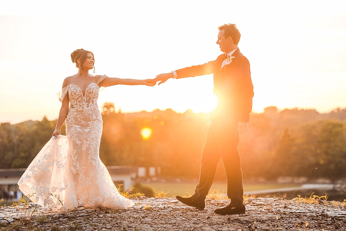 Melicia and Justin reach toward each other in a playful sunset portrait on the rocky shoreline.