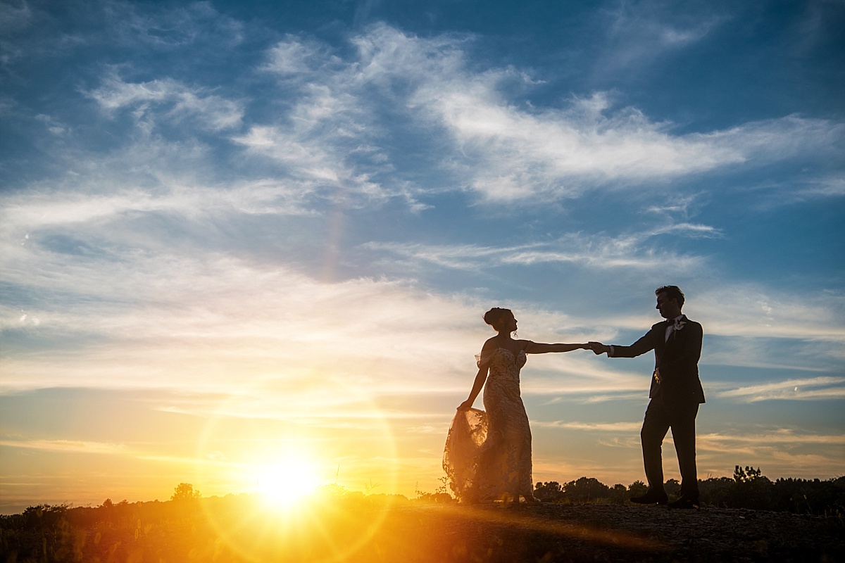 Melicia and Justin hold hands in silhouette against a dramatic sunset sky at Sunset Bluffs.