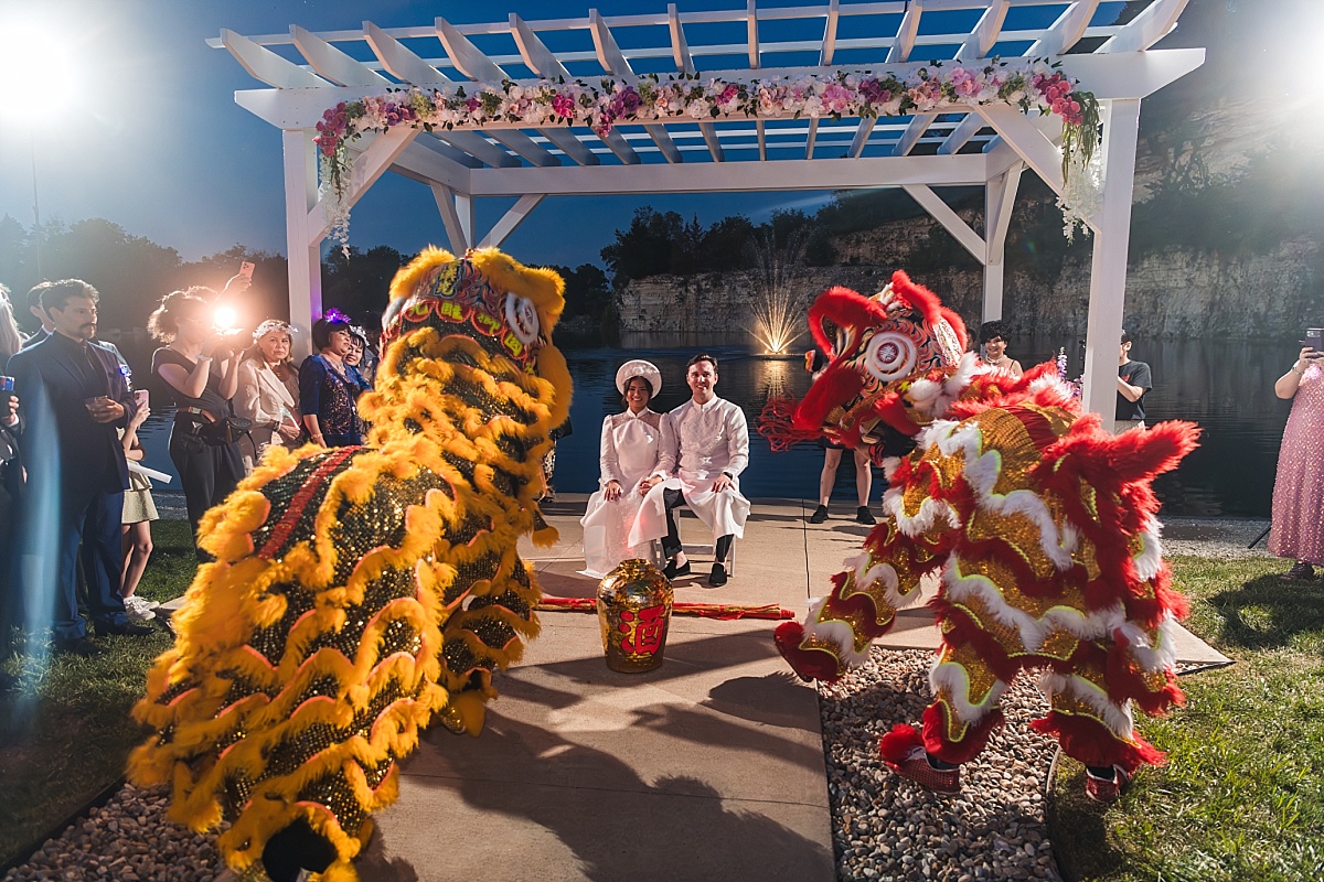 Red and yellow lion dancers perform around Melicia and Justin beneath the flower-covered pergola.