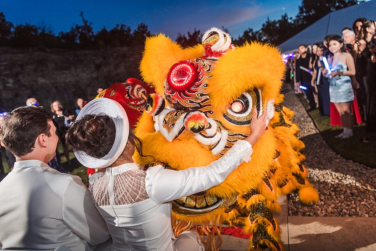 Melicia greets a brightly colored yellow lion dancer during the celebration, with Justin and guests watching nearby.