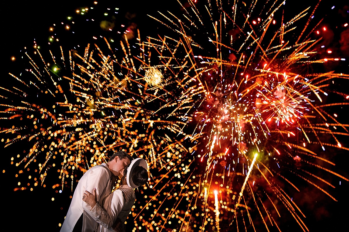 Melicia and Justin kiss beneath a spectacular display of colorful fireworks at their wedding.