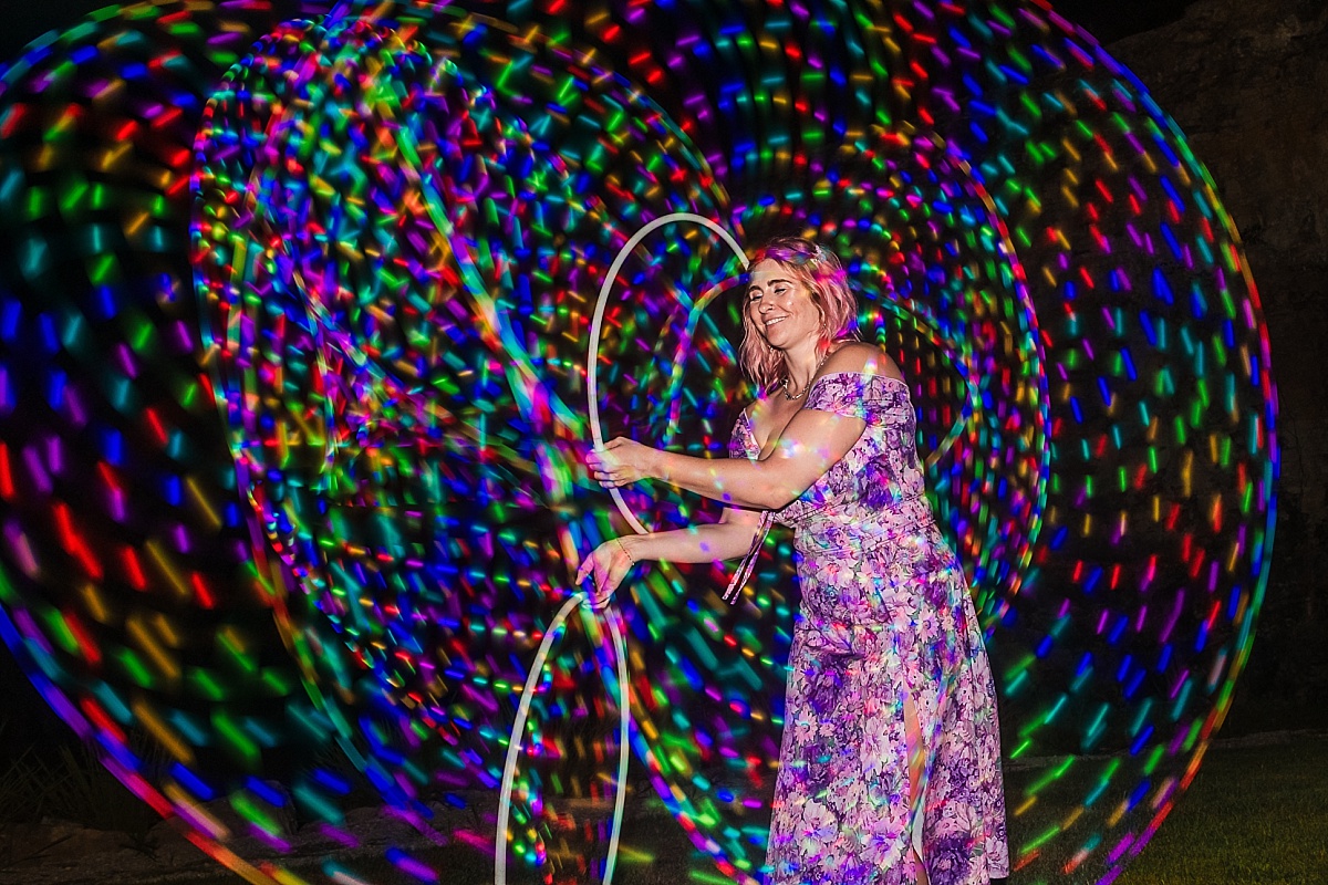 A wedding guest spins illuminated props to create swirling rainbow light trails during the reception.