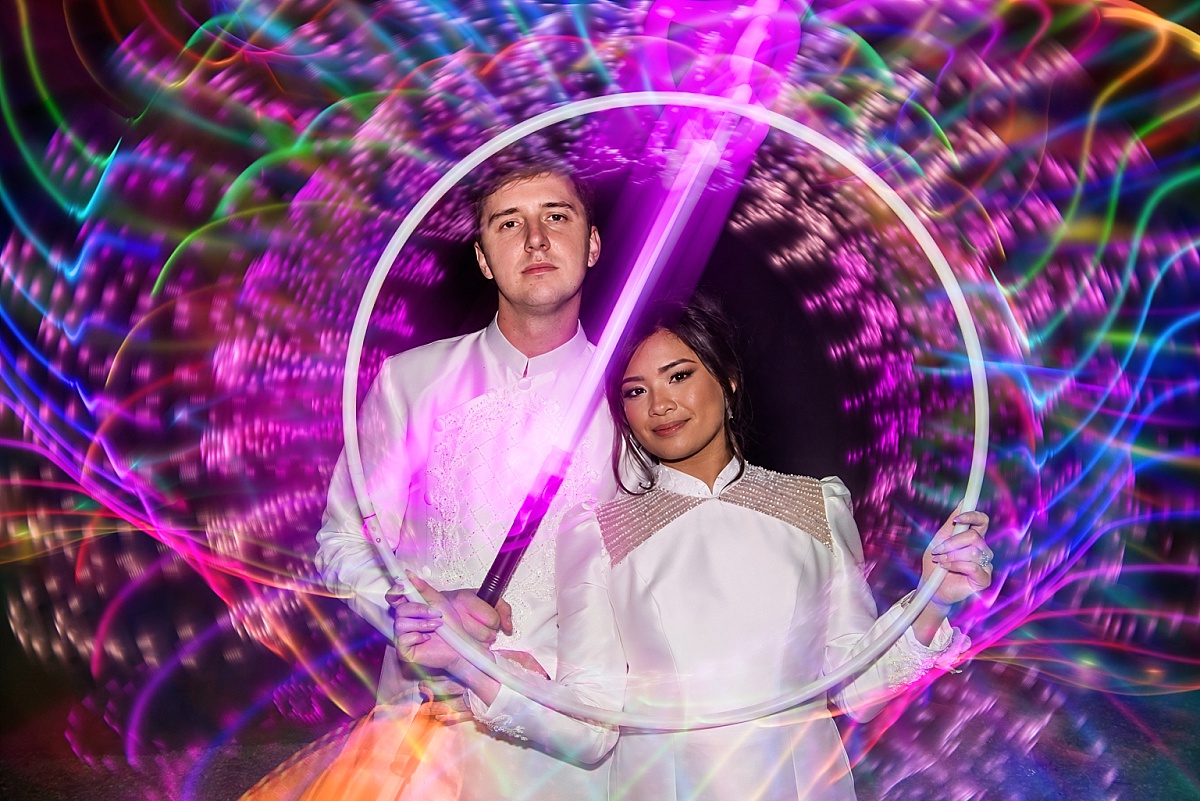 Melicia and Justin pose together inside a circle of colorful light trails created with illuminated props.