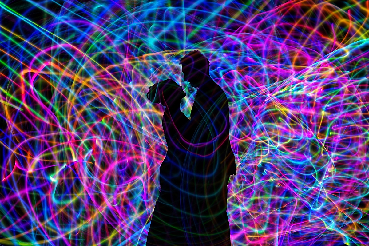 Silhouettes of Melicia and Justin embrace amid vibrant blue, green, purple, and red light trails in a creative wedding portrait.